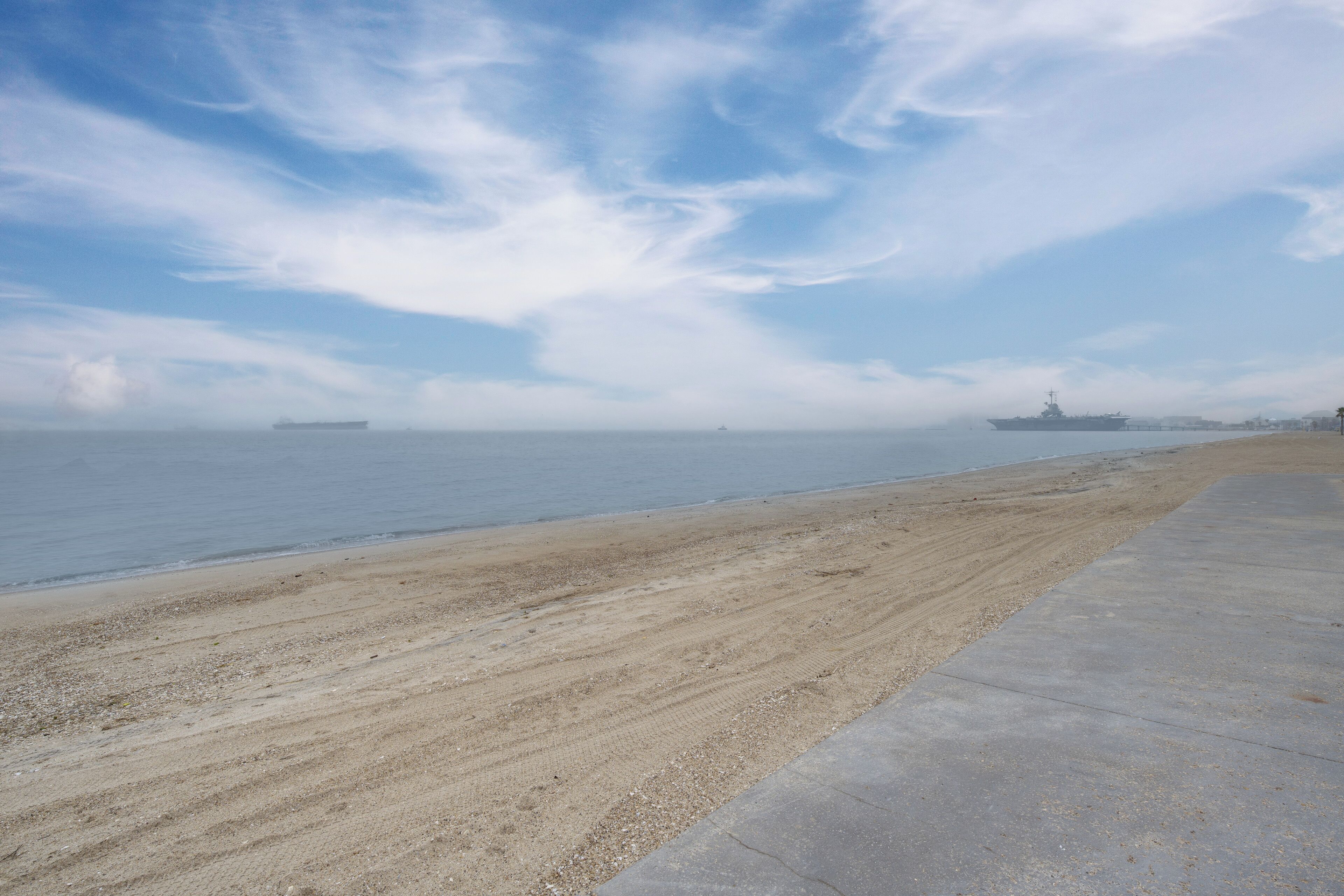 Une plage avec une promenade en béton et un navire visible au loin.