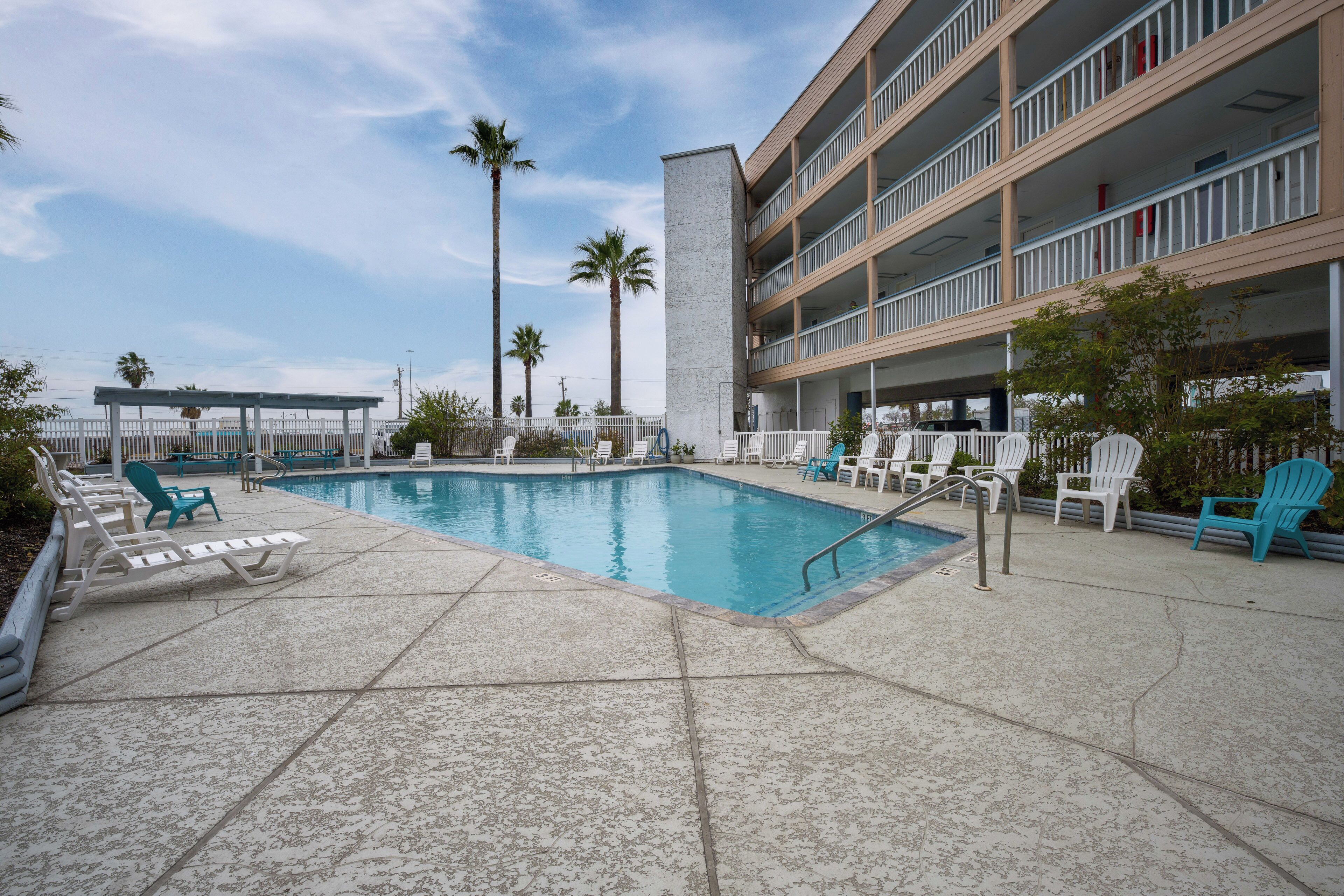 A pool area with lounge chairs, a building with balconies, and palm trees.