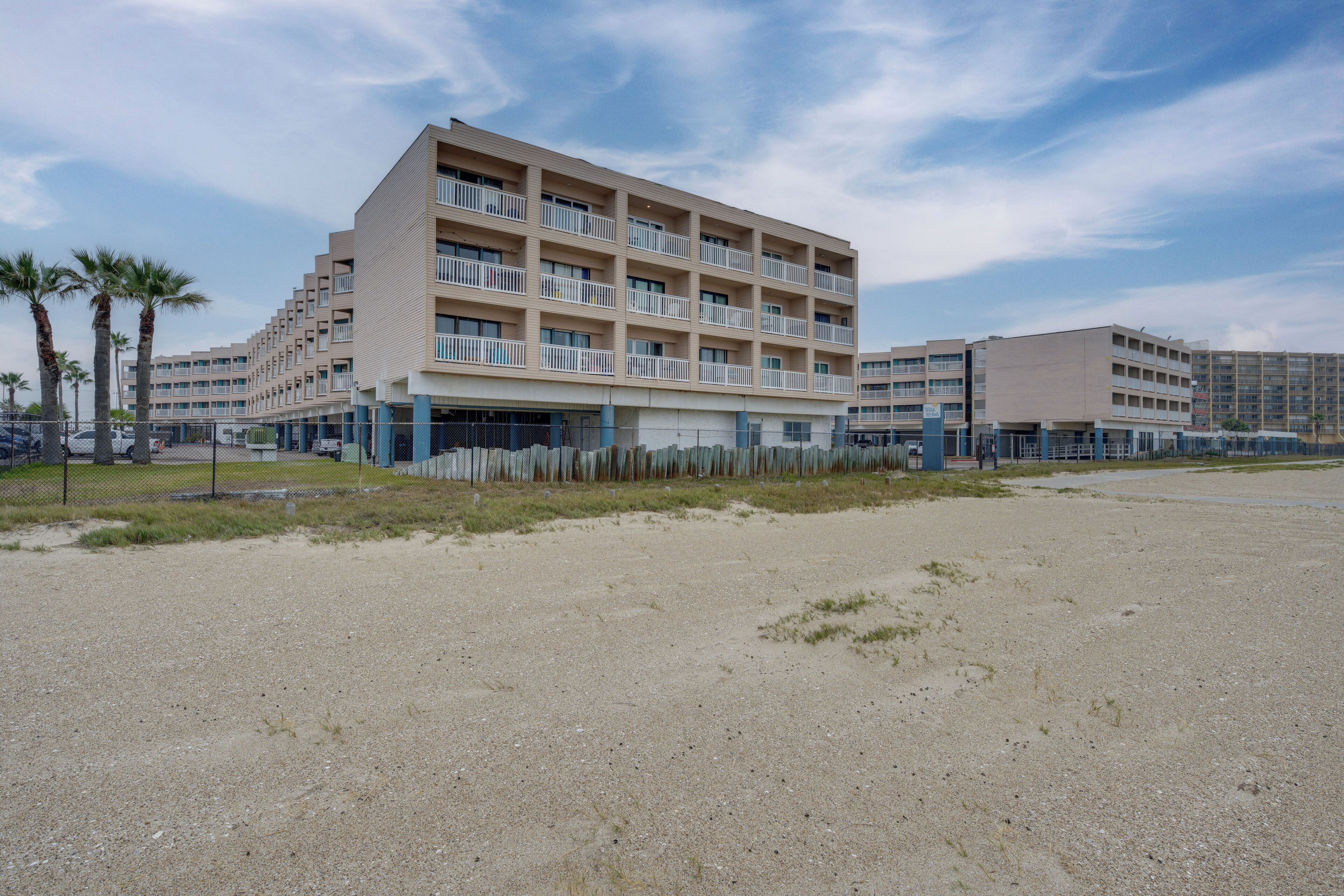 A multi-story hotel with a flat roof, balconies, and a parking area in front.