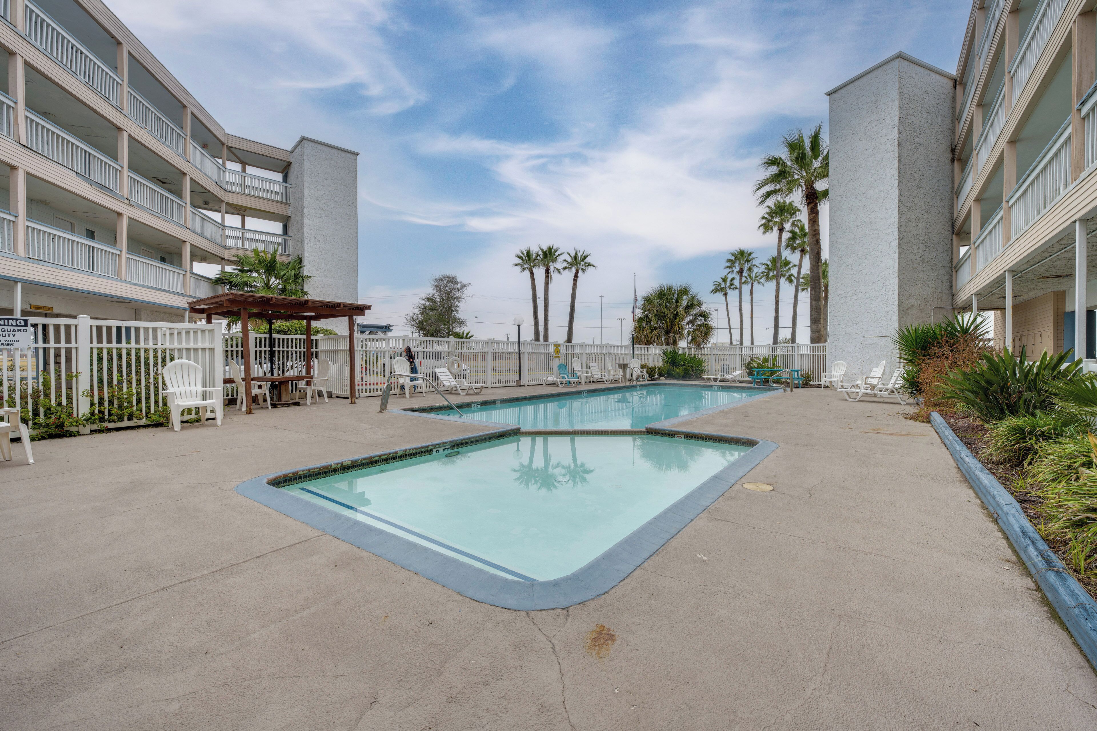 Un espace piscine d’hôtel comprenant deux piscines rectangulaires, des chaises longues blanches et des palmiers.