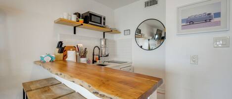 A kitchen with a wooden countertop, white tiles, a microwave, and a sink.
