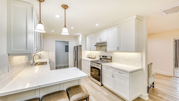 A modern kitchen with white cabinetry, a large island with bar stools, stainless steel appliances, and pendant lighting. - Patio & Workspace: Peaceful Riverside Apartment! (Riverside)