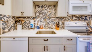 Een keuken met witte kasten, een decoratieve spatwand, een magnetron, een fornuis en een vaatwasser.