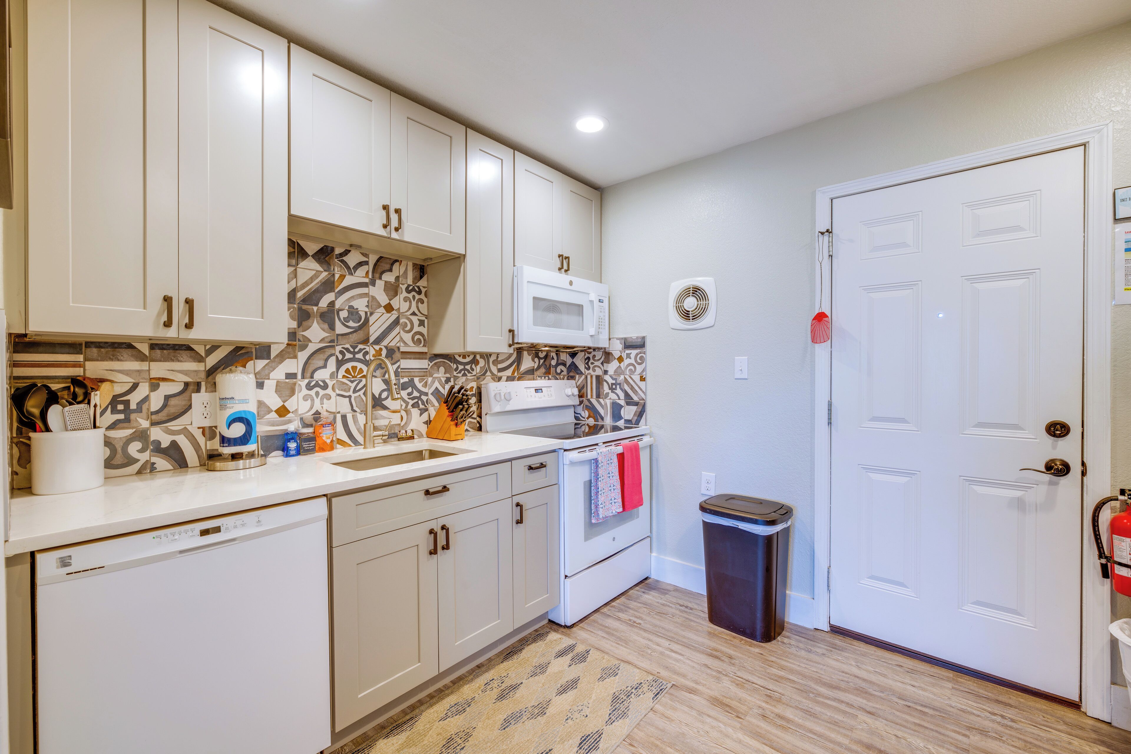 A kitchen with white cabinets, a microwave, a stove, and a trash bin.