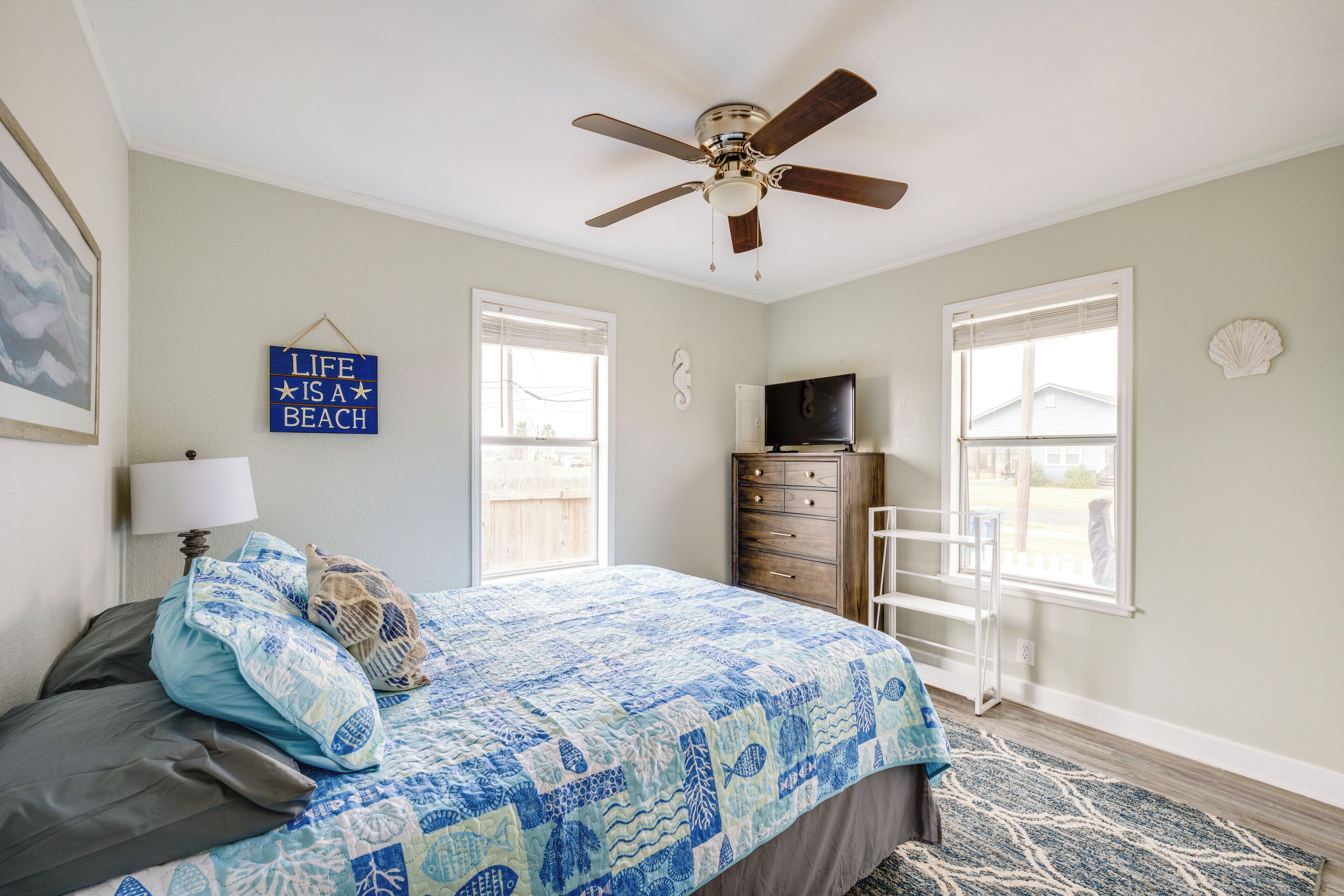 Une chambre à coucher comprenant un lit, un ventilateur de plafond, une commode et deux fenêtres.