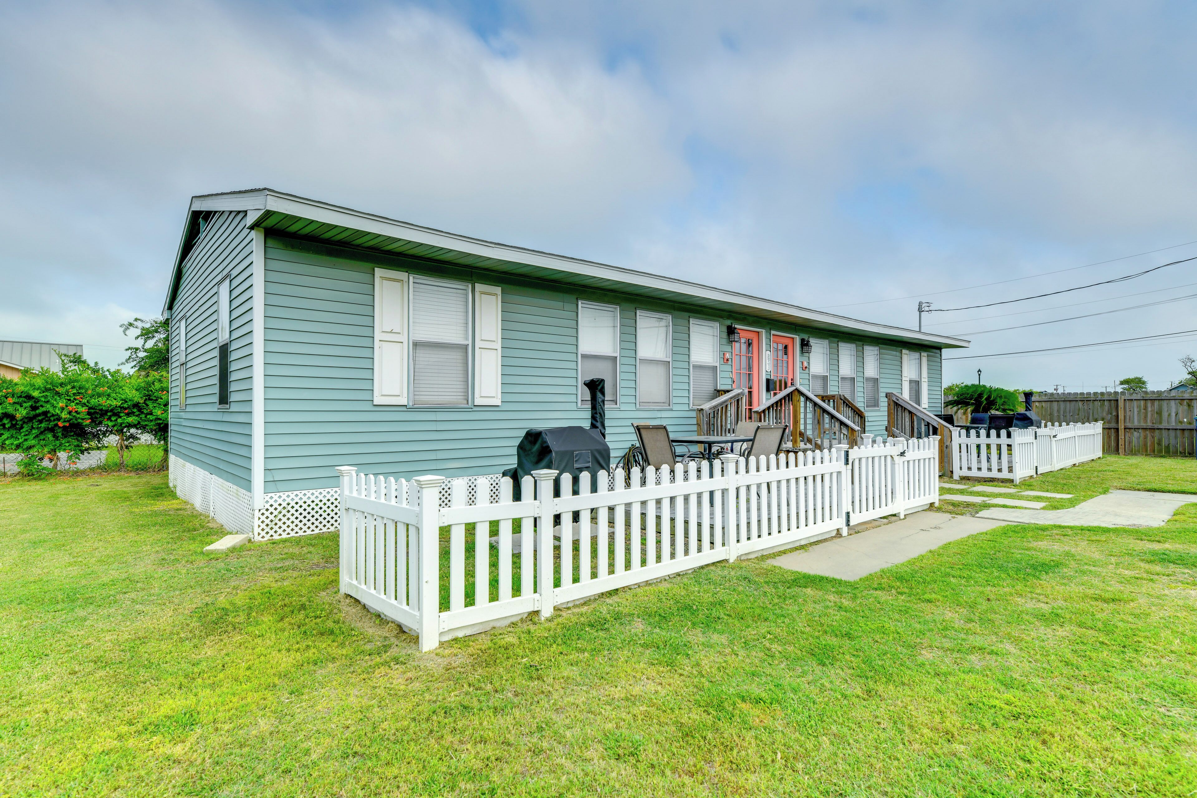 A single-story house with a white picket fence, a covered patio area with outdoor furniture, and a red door.