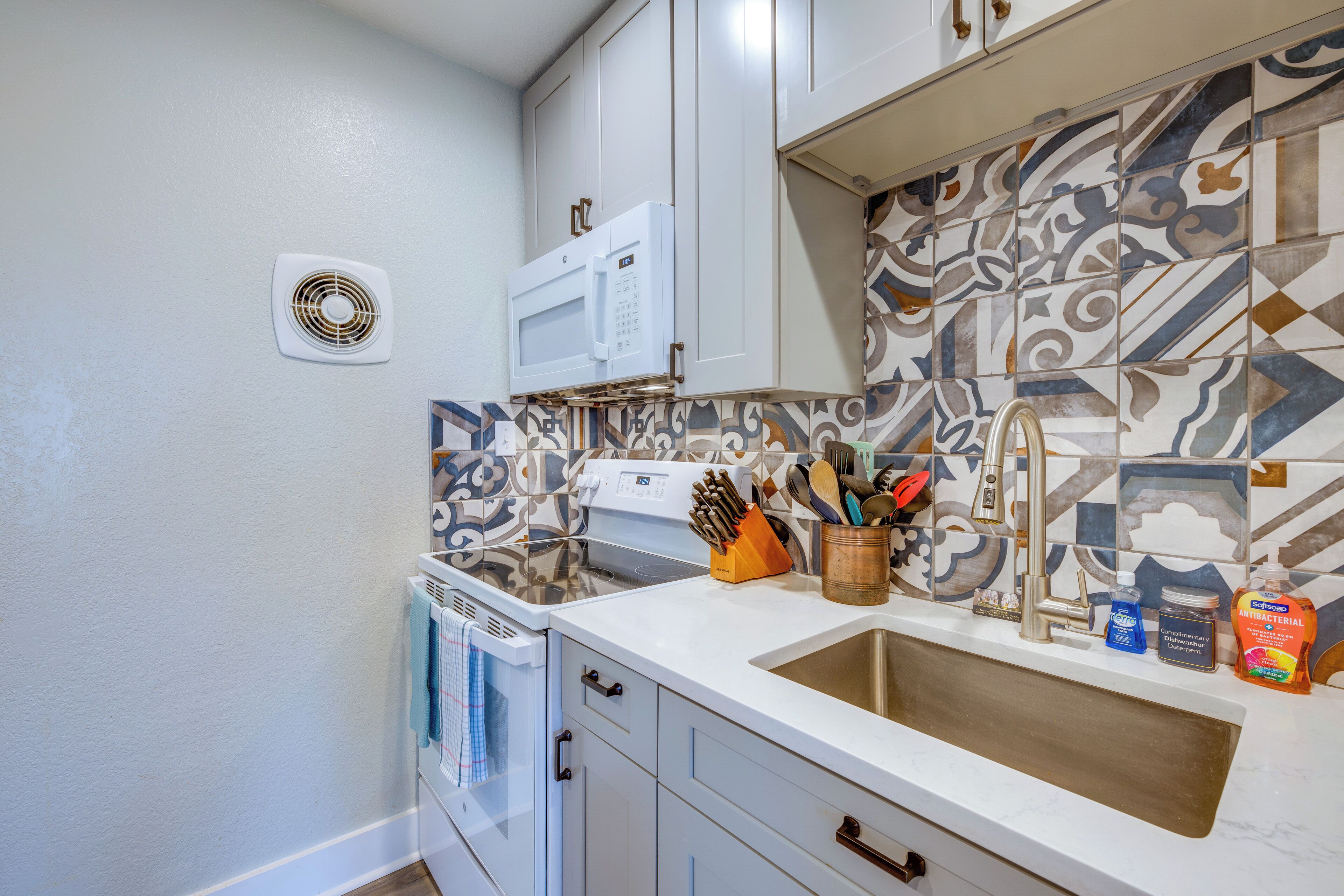 A kitchen with white cabinets, a microwave, a sink with a modern faucet, and a patterned backsplash.