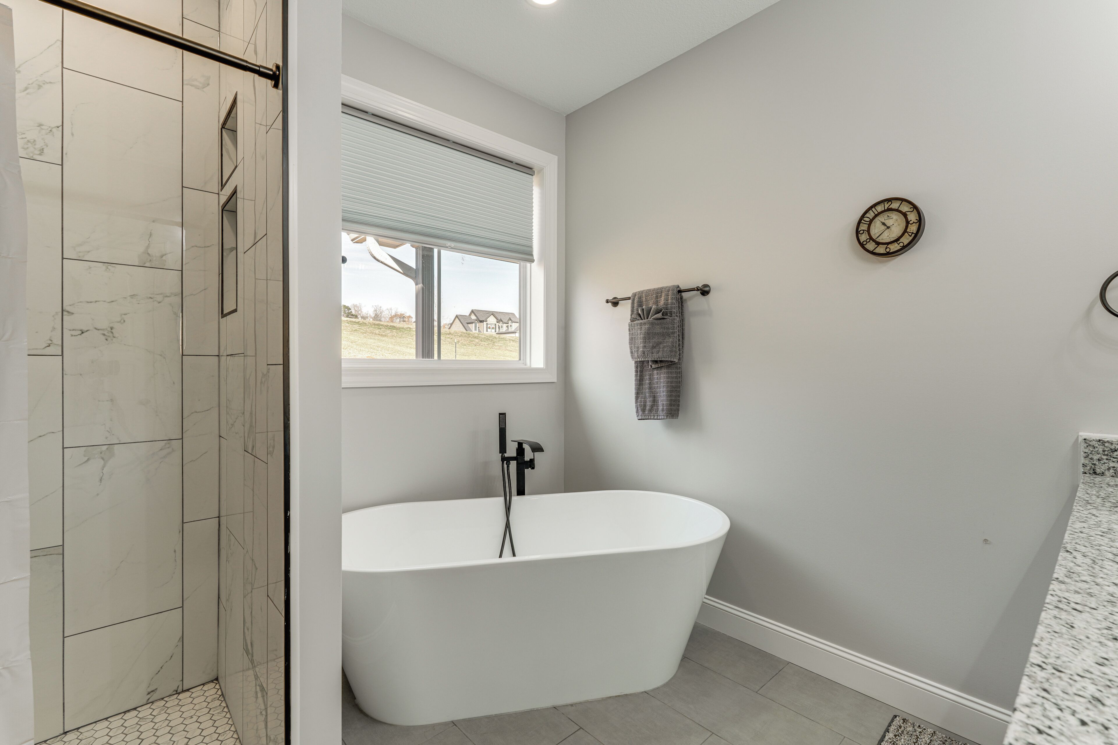 A modern bathroom with a freestanding bathtub, a shower area, and a window providing a view of the outdoors.