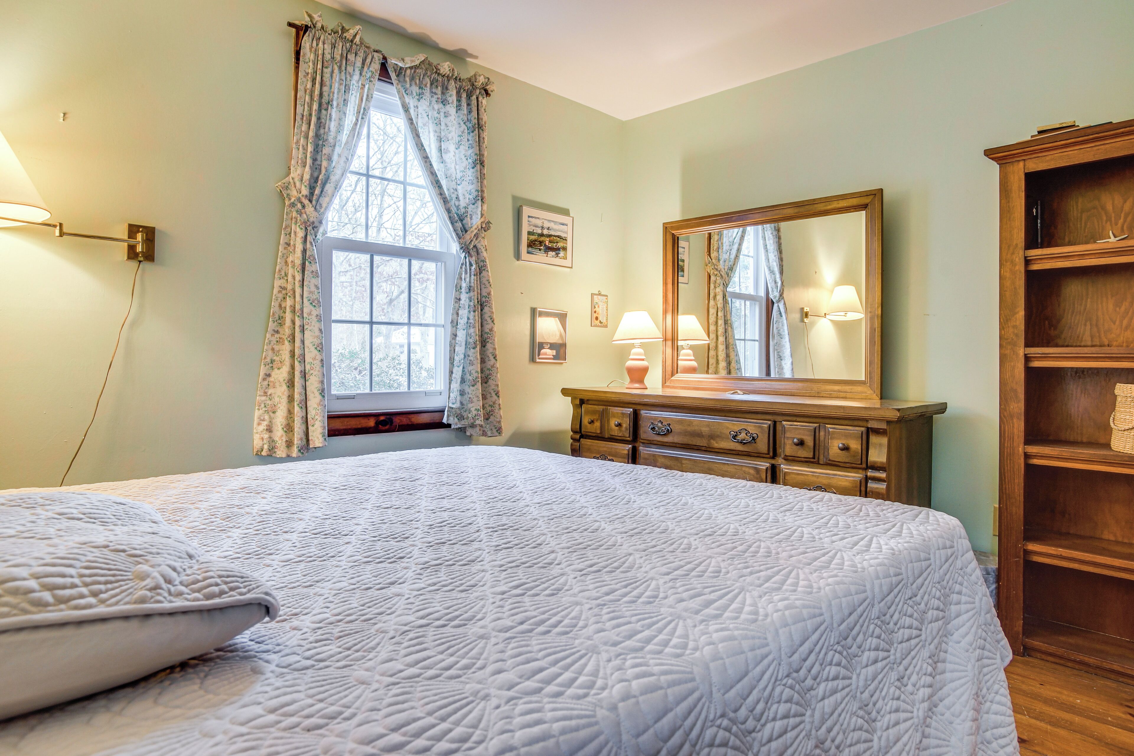 A bedroom with a large bed, a dresser, a mirror, and a window with curtains.