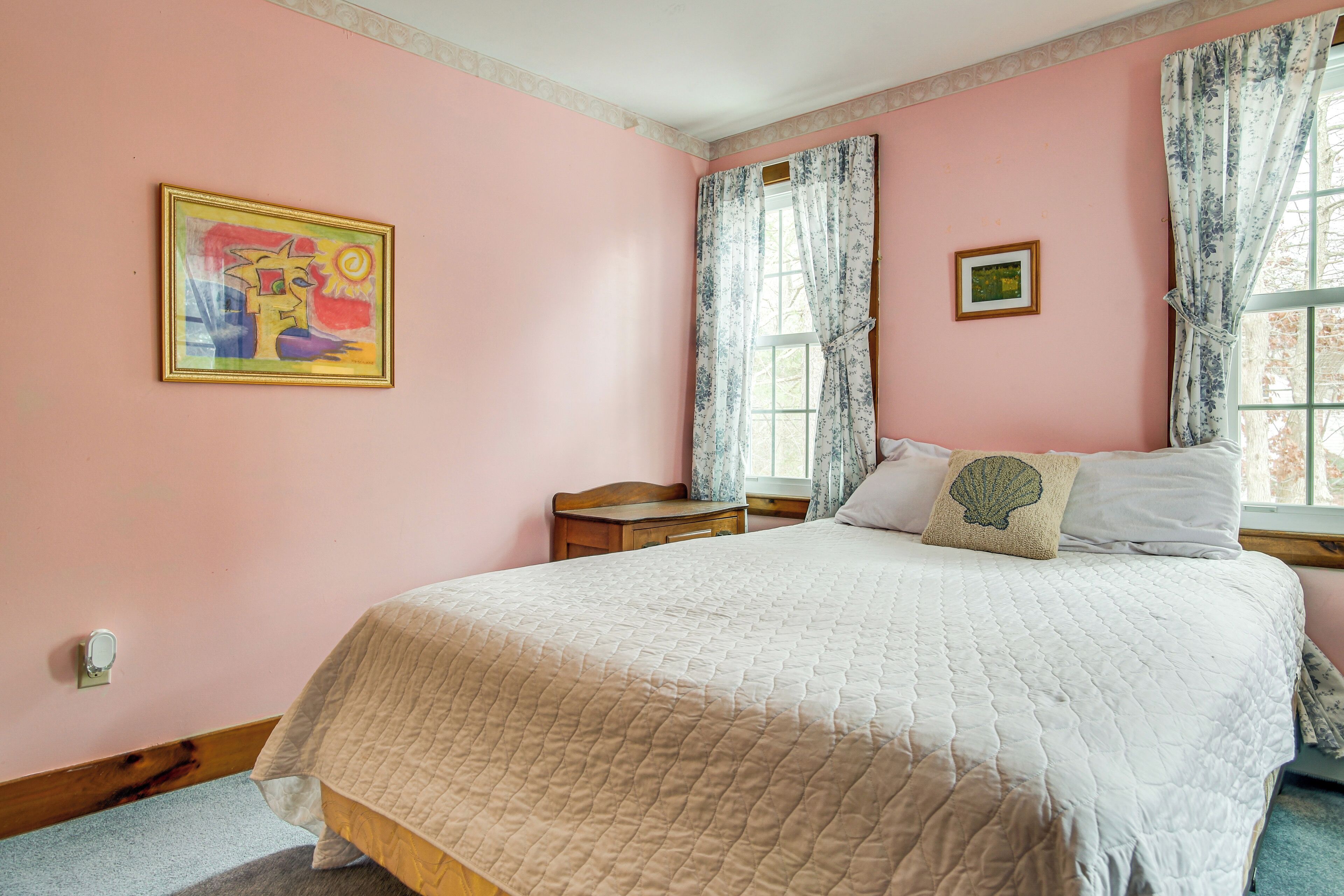 Une chambre à coucher avec un grand lit, une table de chevet, une fenêtre ornée de rideaux à motifs floraux et un tableau accroché au mur.