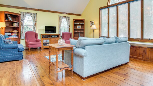 A living room with a blue sofa, a red armchair, a wooden coffee table, and a television. - Beach Days & Nautical Adventures: Cotuit Home (Cotuit)