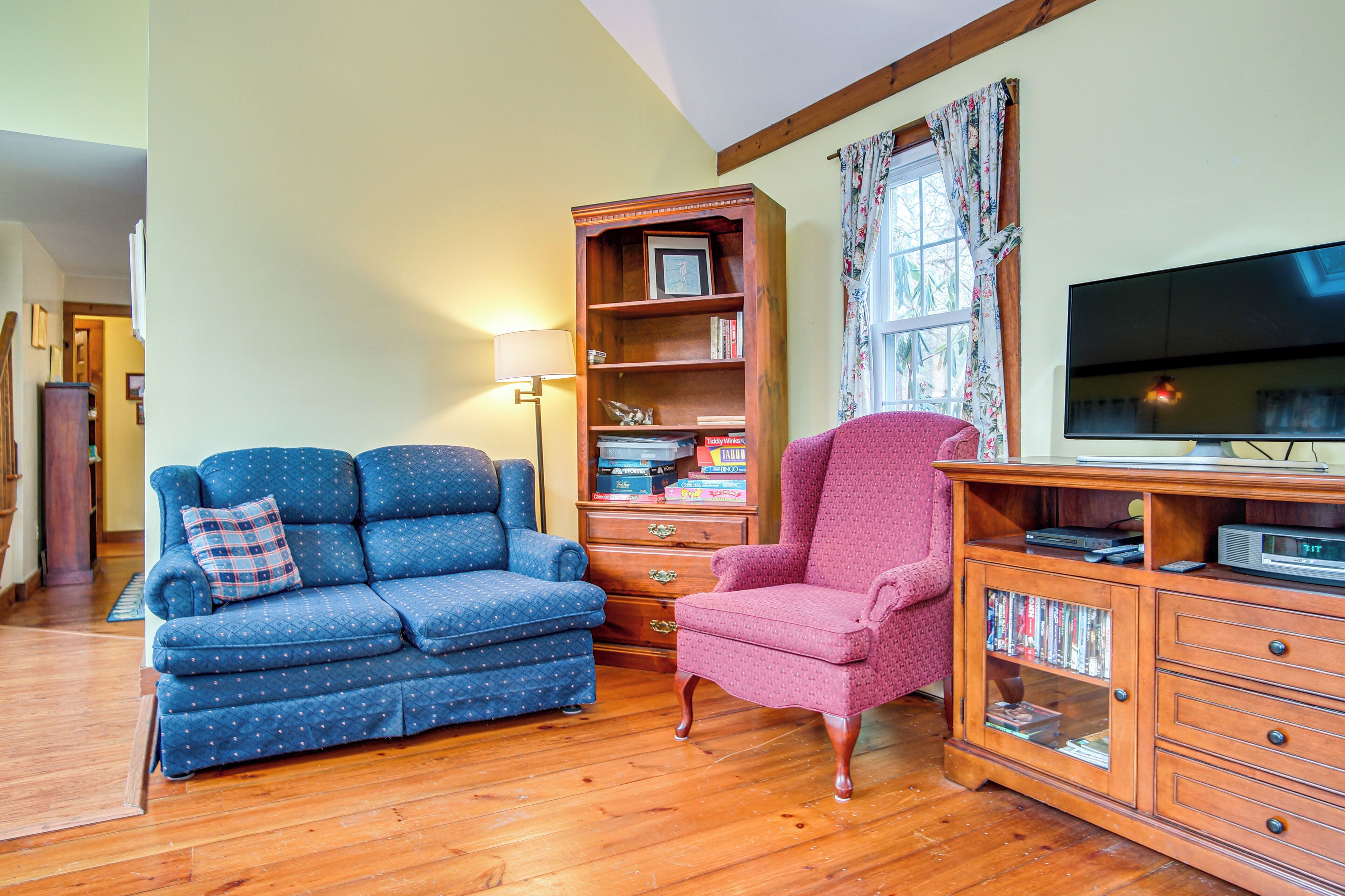 A living room with a blue sofa, a pink armchair, a wooden cabinet with a TV, and a bookshelf.