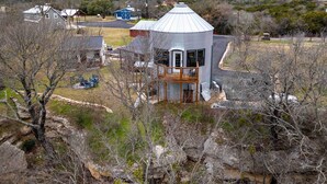A unique, cylindrical building with a balcony, surrounded by trees and a few other structures in a rural setting. - Tin De Blue Grainbury Silo and Cabins (Weatherford)