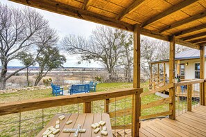 Eine Holzterrasse mit Blick auf eine ländliche Landschaft, ein Tisch mit Dominosteinen und blaue Stühle.
