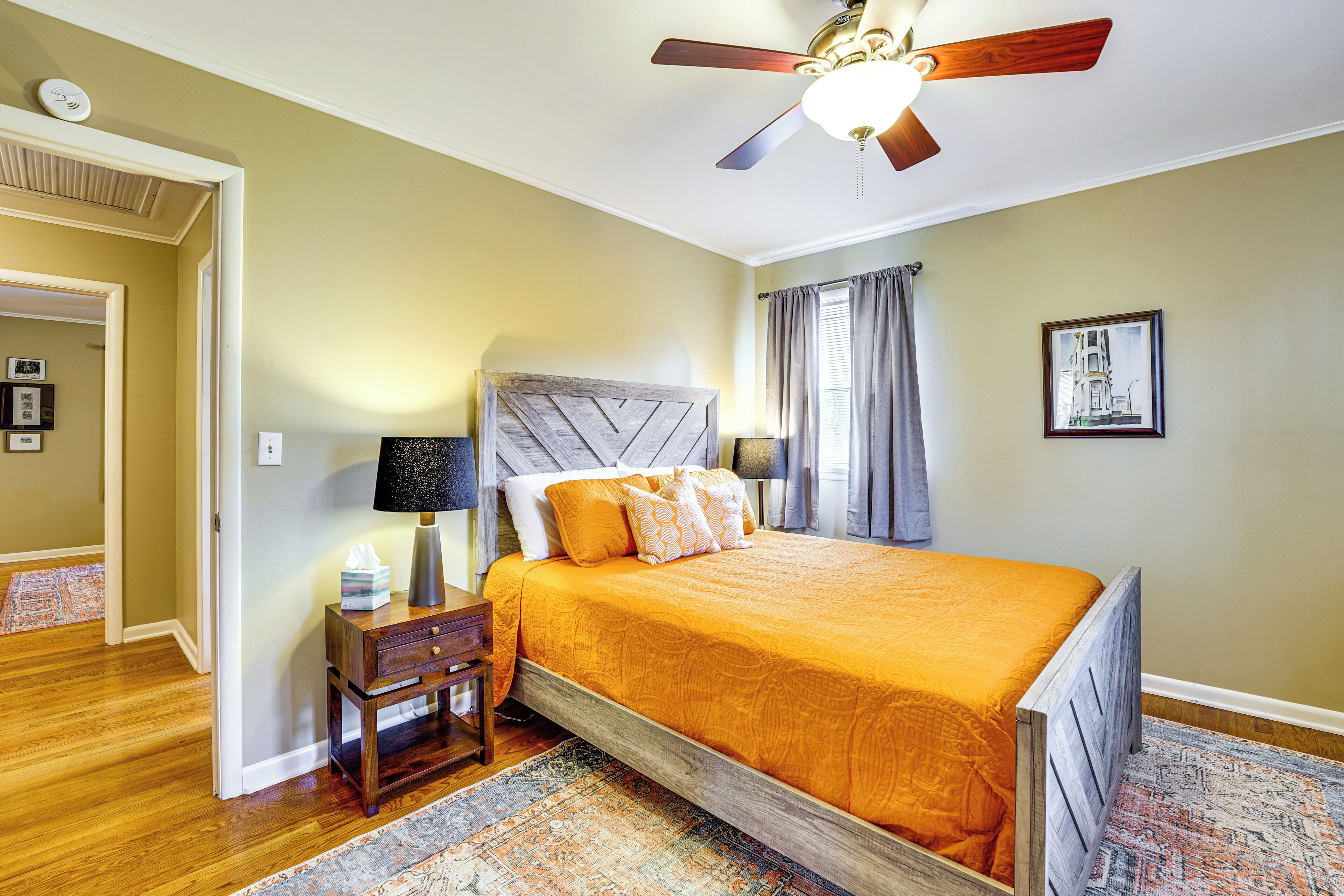 A bedroom with a wooden bed, a nightstand, a lamp, a ceiling fan, and a rug.