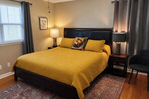 Une chambre d’hôtel avec un lit, une table de chevet, une lampe, une chaise et une fenêtre avec des rideaux.