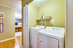 Un lavadero con dos lavadoras y secadoras de carga frontal, un estante con productos de limpieza y una puerta que da a otra habitación.