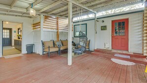 Une véranda couverte avec un plancher en bois, une porte rouge et une chaise suspendue.