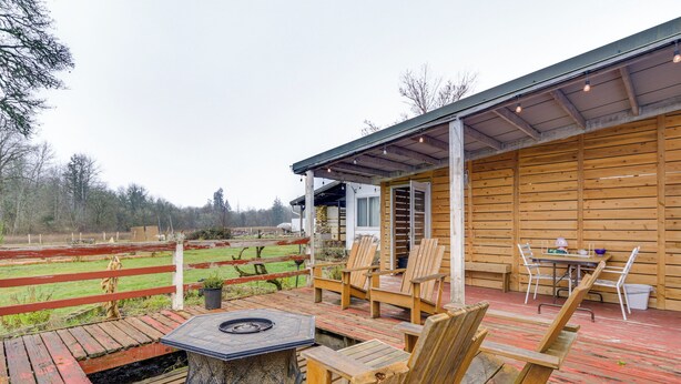 Une terrasse en bois avec des meubles d’extérieur, un foyer et une vue sur un champ clôturé.