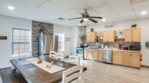 A modern kitchen with wooden cabinets, a stainless steel refrigerator, a microwave, and a ceiling fan.