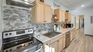 A modern kitchen with a stainless steel range hood, wooden cabinets, a tiled backsplash, and a marble countertop.