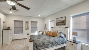 A bedroom with a bed, bedside table, ceiling fan, and artwork on the walls.