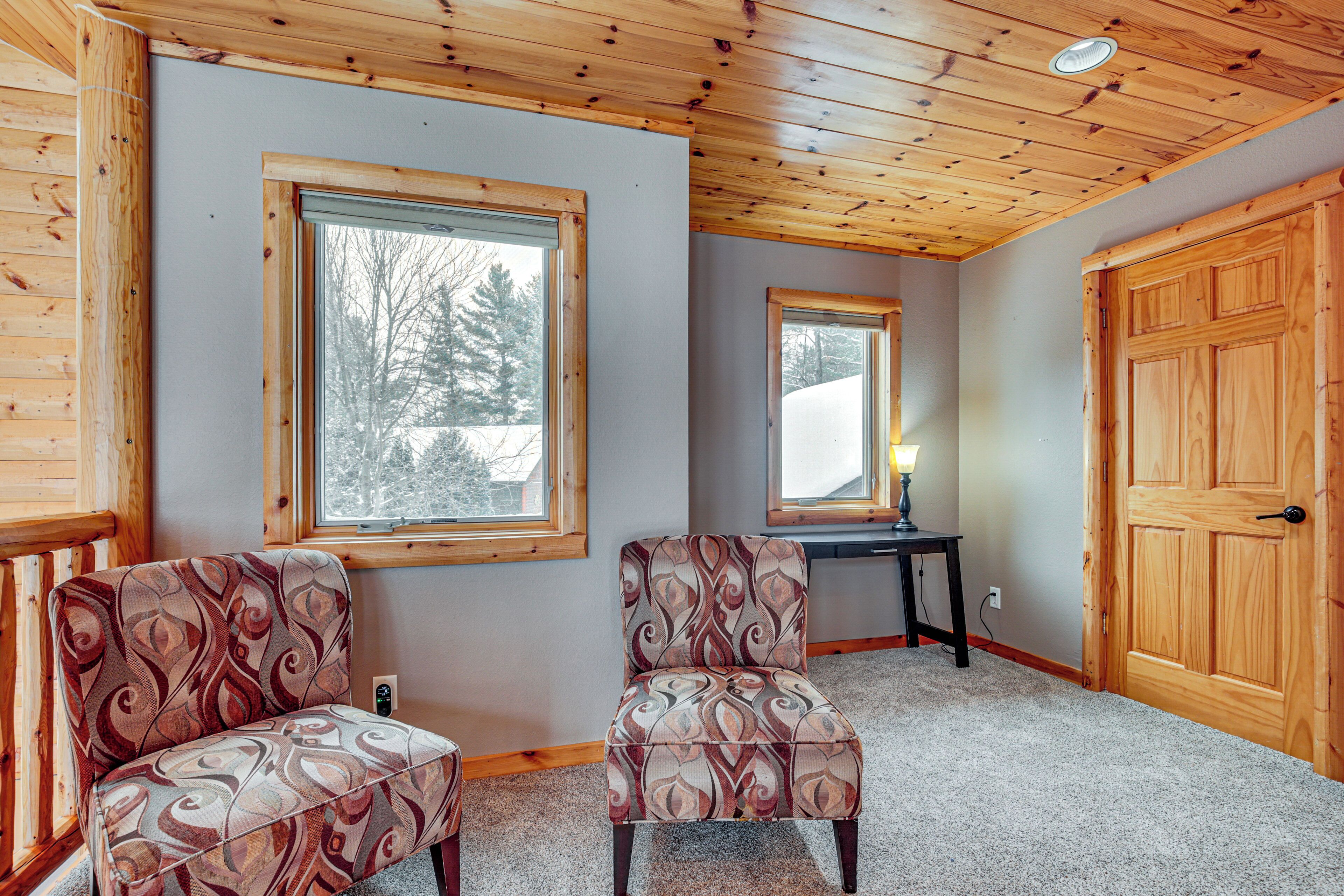 A room with two patterned armchairs, a wooden door, and a window with a view of trees.