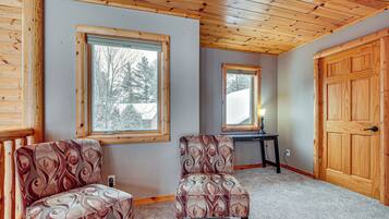A room with two patterned armchairs, a wooden door, and a window with a view of trees.
