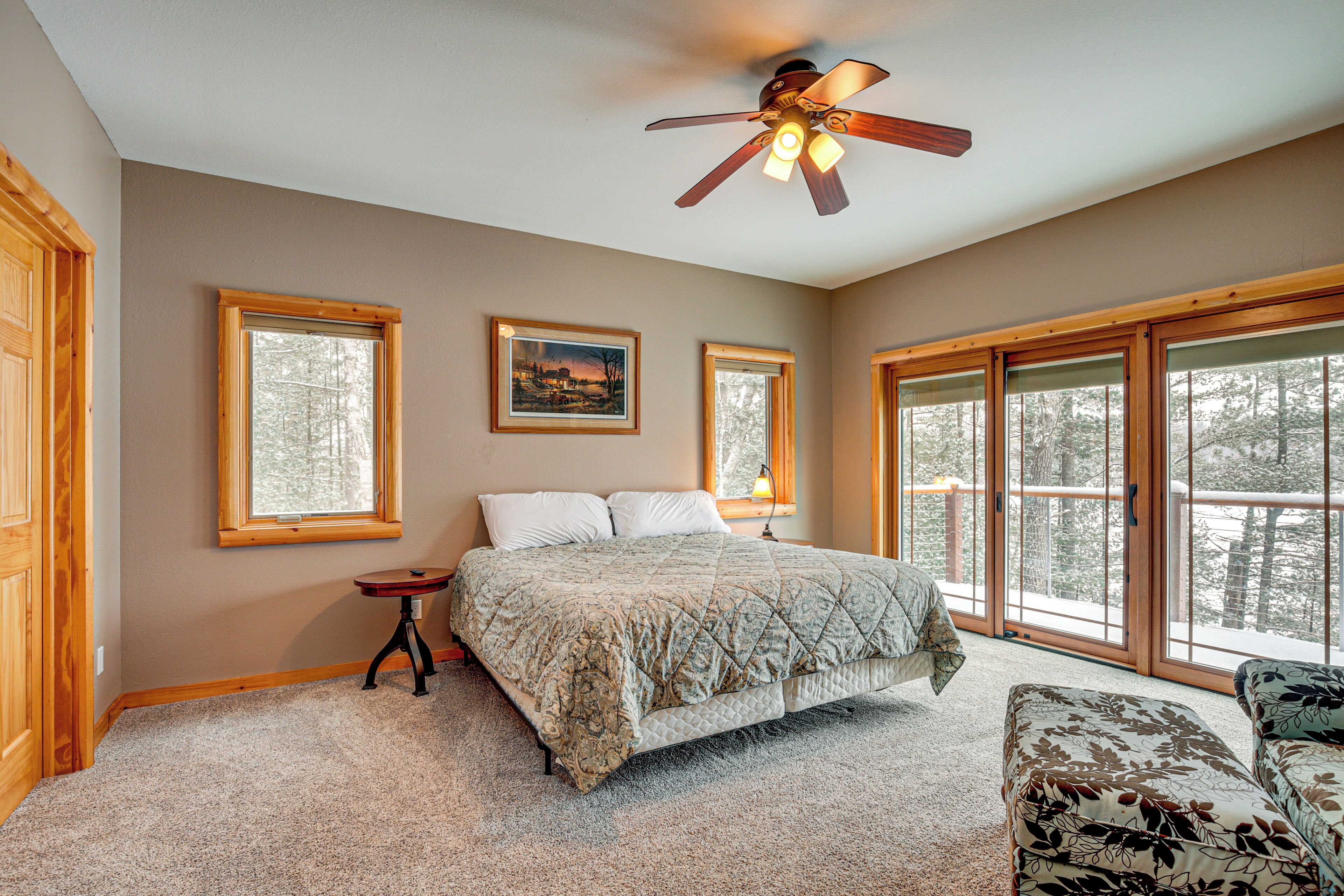 A bedroom with a bed, a nightstand, a chair, and a ceiling fan. There are large windows and a door.