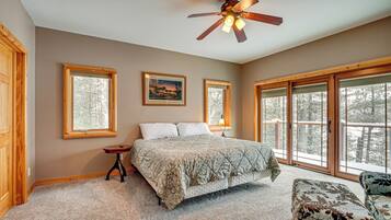 A bedroom with a bed, a nightstand, a chair, and a ceiling fan. There are large windows and a door.