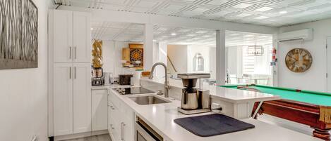 A modern kitchen with white cabinetry, a coffee maker, and a pool table.