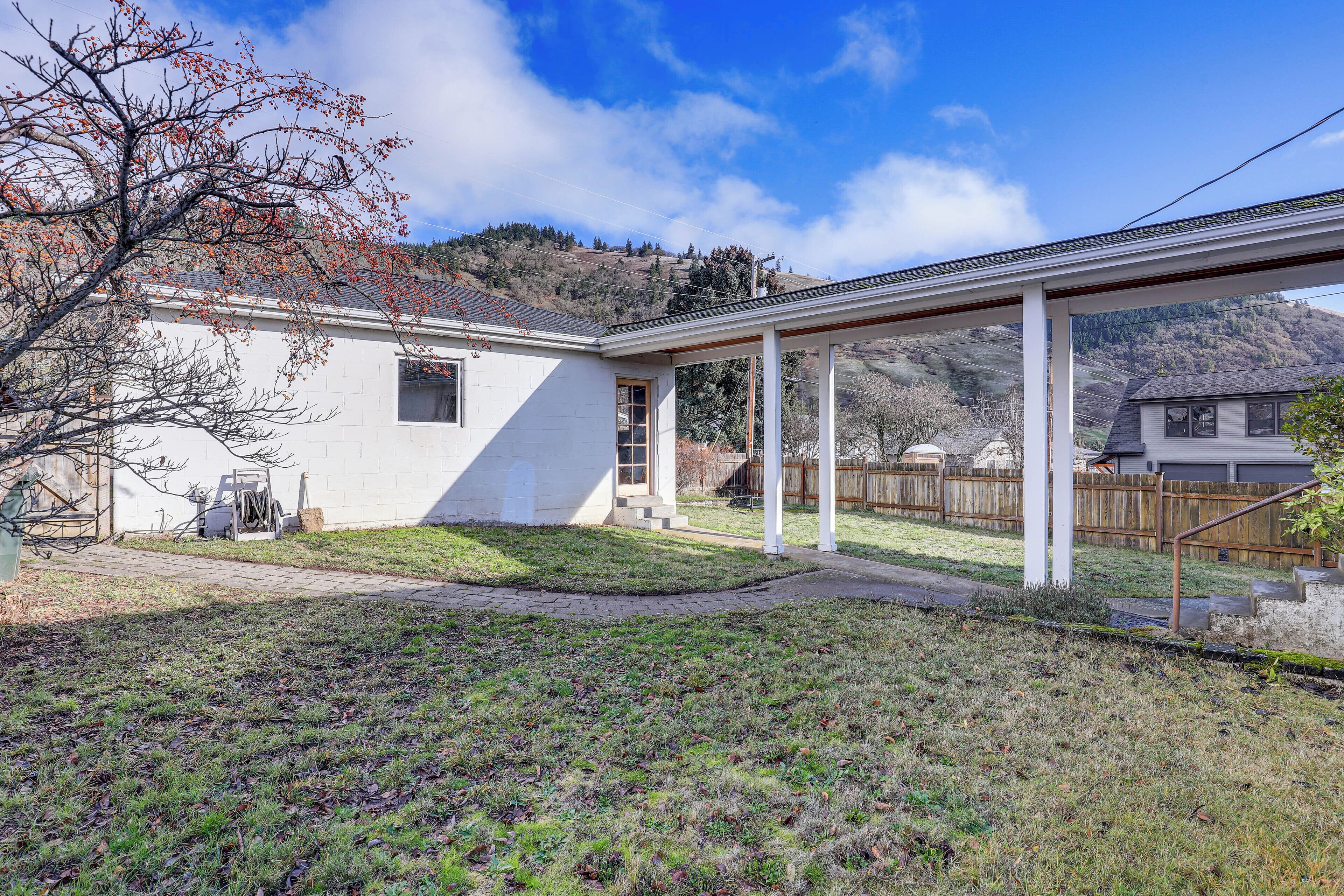 A house with a covered patio, a small yard, and a hilly landscape in the background.
