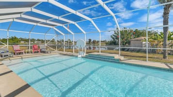 A covered swimming pool with a basketball hoop, red chairs, and a view of the surrounding area.