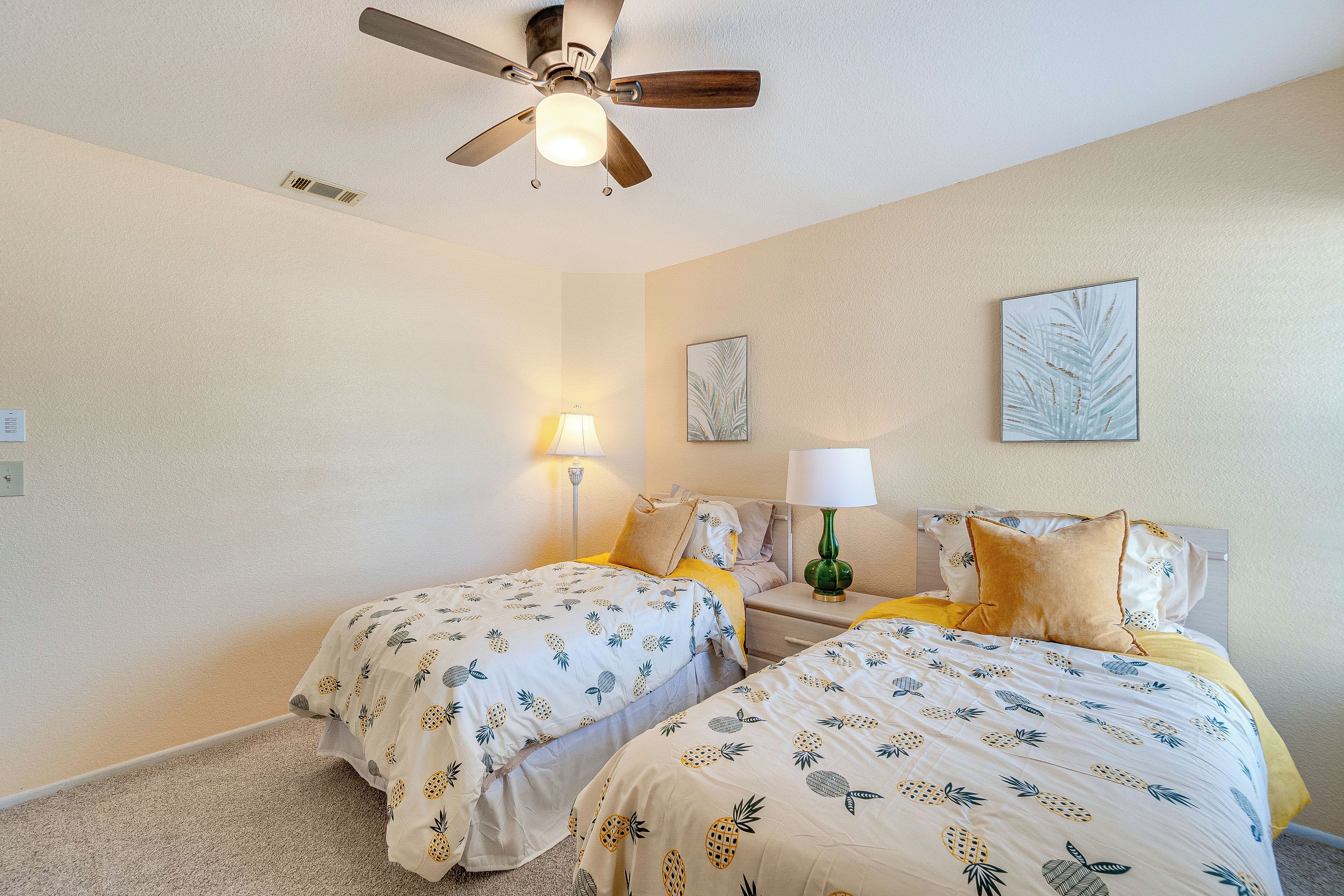 A bedroom with two beds, a ceiling fan, wall-mounted lamps, and artwork.
