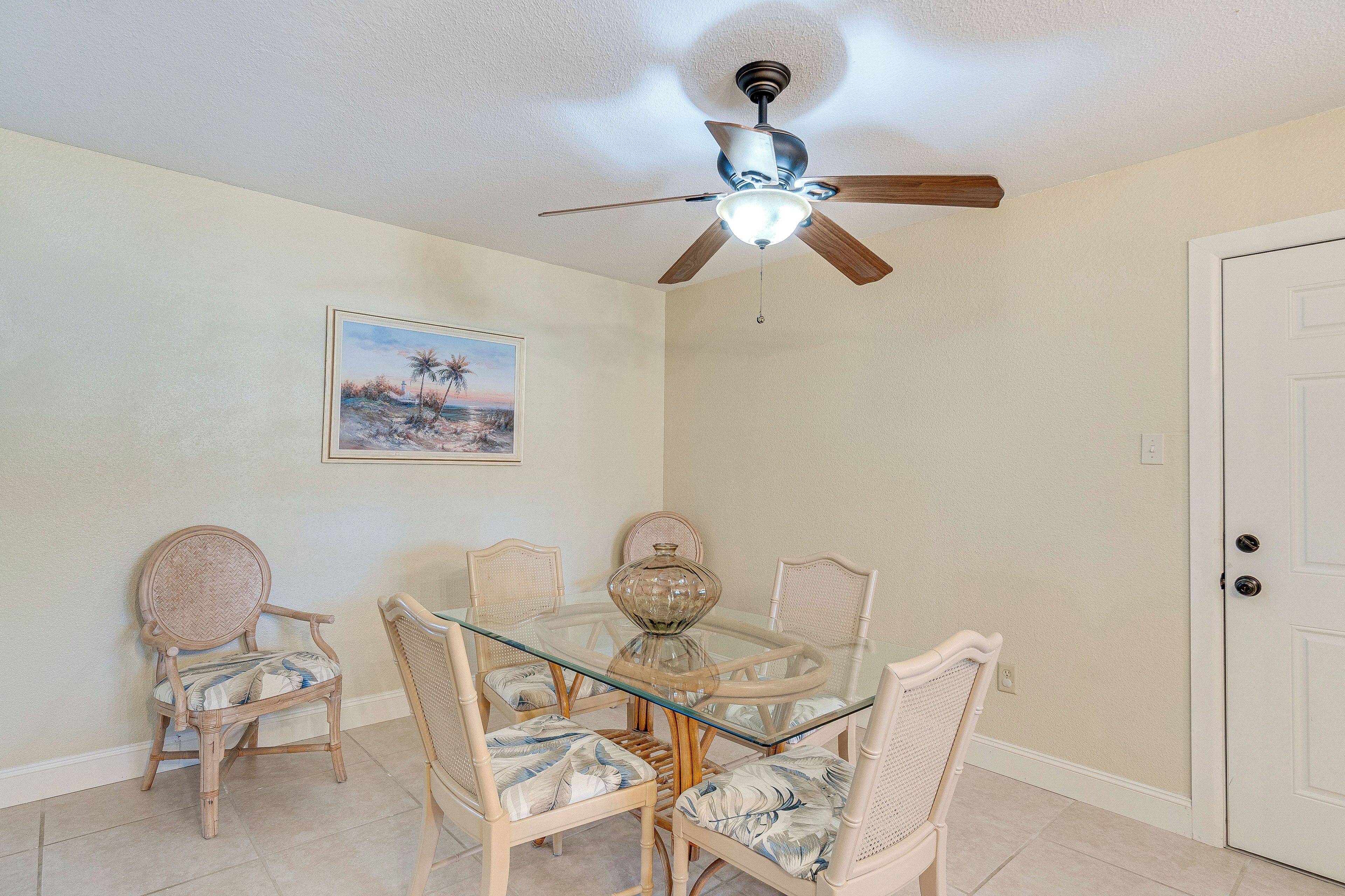 A dining area with a glass table, wicker chairs, a ceiling fan, and a door.
