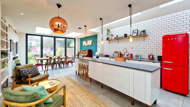Una cocina moderna con una isla central, un refrigerador rojo y un comedor con vistas a un jardín.