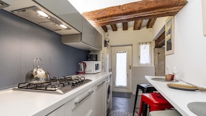 A compact kitchen with a gas stove, microwave, and a washing machine. There are red stools and a white countertop. - Ca Nova II by Wonderful Italy (Venecia)