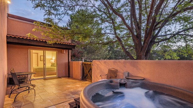 Un bain à remous installé dans un espace patio, avec une table et des chaises, une porte et un arbre en arrière-plan.