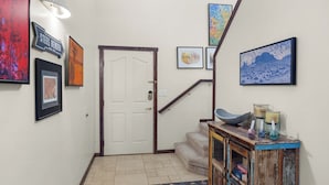 Un couloir avec une porte blanche, un escalier et une console en bois ornée de bougies et d’objets décoratifs.