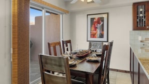 Un coin repas avec une table en bois dressée pour quatre personnes, un ventilateur de plafond et une œuvre d’art encadrée accrochée au mur.