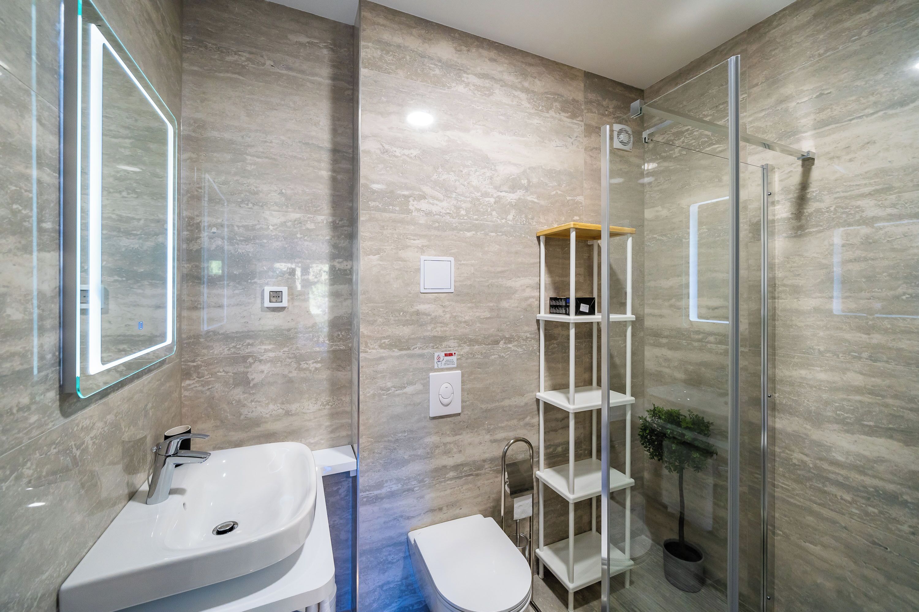 Une salle de bain moderne avec un grand lavabo, une cabine de douche en verre et une petite étagère.