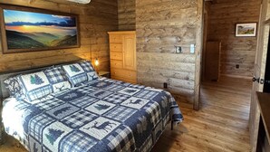 A wooden cabin bedroom with a bed, a nightstand, a dresser, and a painting of a landscape. - Rocking on Heaven's Door-Covered Porch -  WIFI - Gas Grill (Topton)