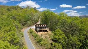 A modern house with a balcony, surrounded by dense forest, and a winding road nearby. - Brook Haven-Mountain Views - Hot Tub - Outdoor Pizza Oven (Bryson City)
