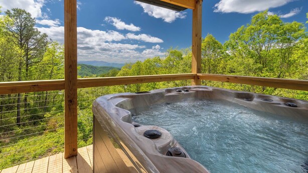 A hot tub with a wooden deck and a view of a forest and mountains. - Brook Haven-Mountain Views - Hot Tub - Outdoor Pizza Oven (Bryson City)