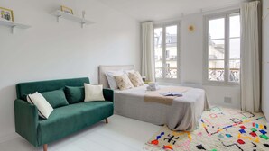 A modern bedroom with a green sofa, a bed with a white duvet, and a colorful rug.