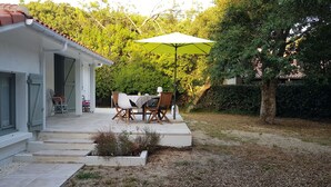 A house with a covered patio, outdoor seating, and a garden area. - Landes house between beach and lake in SOORTS HOSSEGOR, ideal for families (Soorts-Hossegor)