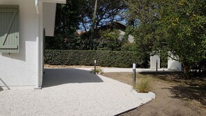 A white building with a covered porch, a chair, and a hedge in the background. - Landes house between beach and lake in SOORTS HOSSEGOR, ideal for families (Soorts-Hossegor)