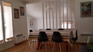 A dining area with a table set for six, black chairs, a striped tablecloth, and a hanging light fixture. - Landes house between beach and lake in SOORTS HOSSEGOR, ideal for families (Soorts-Hossegor)