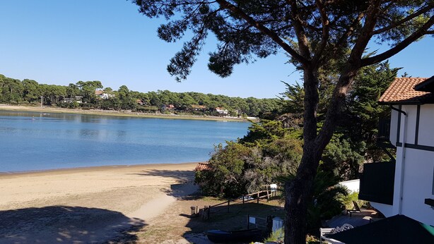 A lakeside property with a white building, a sandy beach, and a clear view of the lake. - Landes house between beach and lake in SOORTS HOSSEGOR, ideal for families (Soorts-Hossegor)