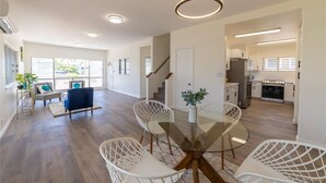A spacious living area with a glass dining table, white wireframe chairs, and a staircase leading to another level.